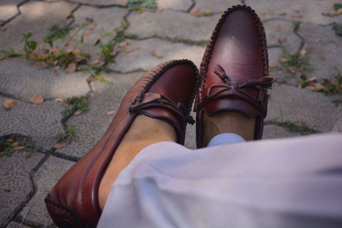 Pair of polished dark brown leather penny loafers worn with tailored trousers