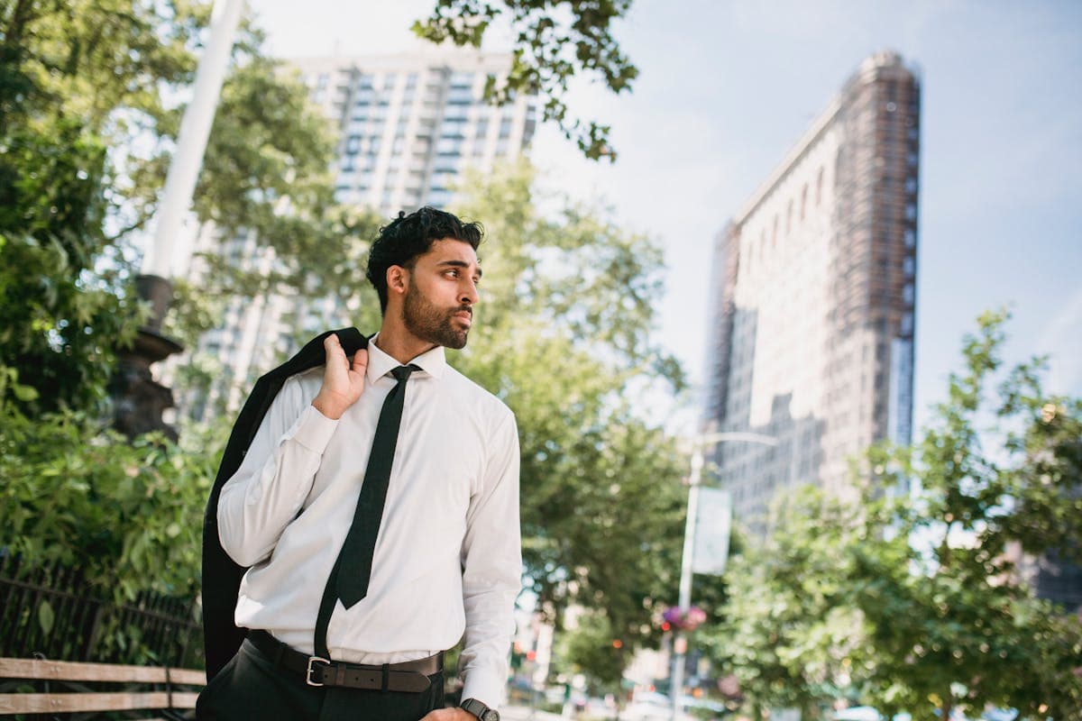 A man in a well-fitted plain black suit and white shirt standing confidently in everyday city surroundings without costume elements