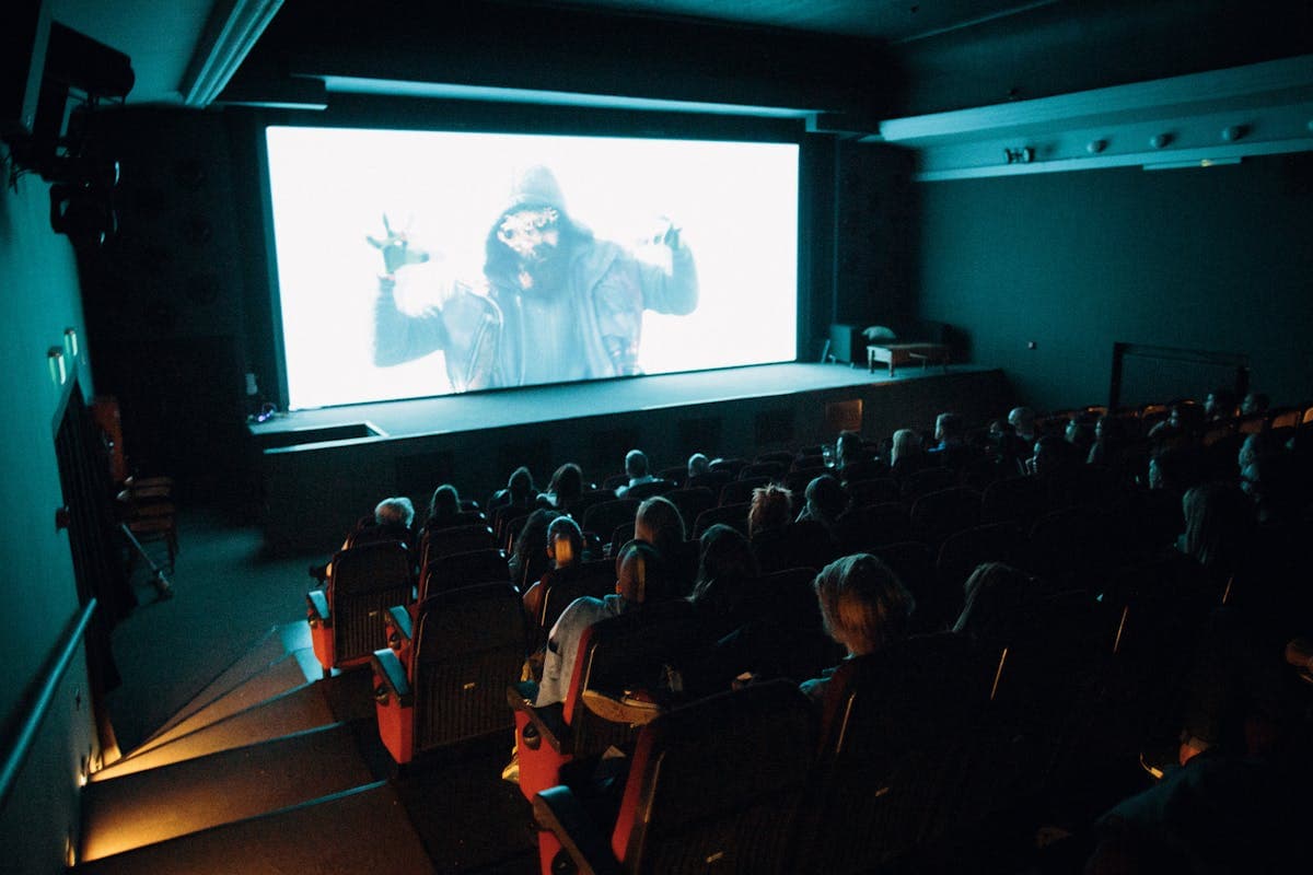 Moviegoers in formal dark suits arriving at a cinema lobby for a premiere screening, treating the night as a dress-up event