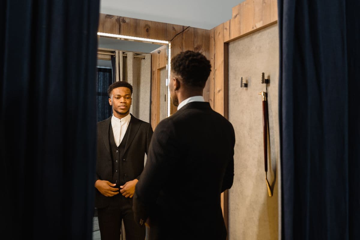 Man adjusting the shoulder of a well-fitted suit jacket in front of a mirror