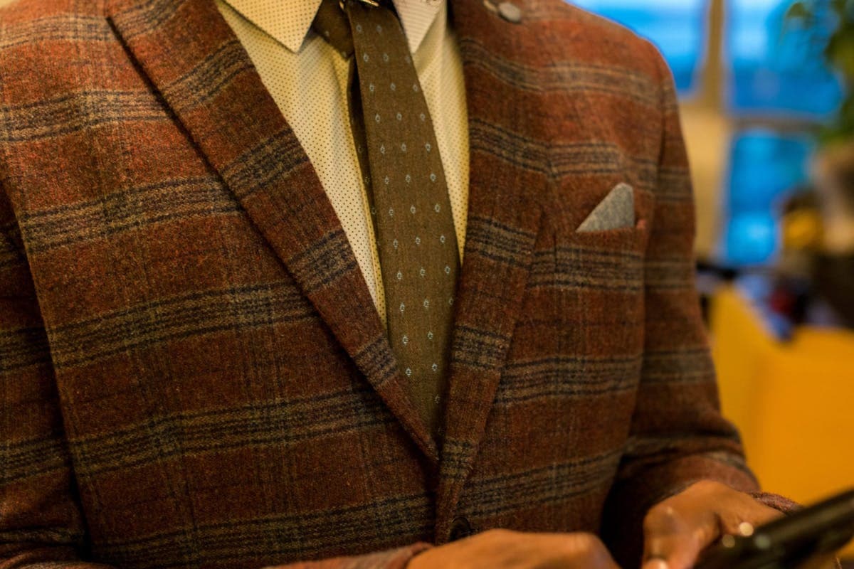 Close-up of a navy suit jacket with notch lapel and a folded white pocket square on a tailor's form
