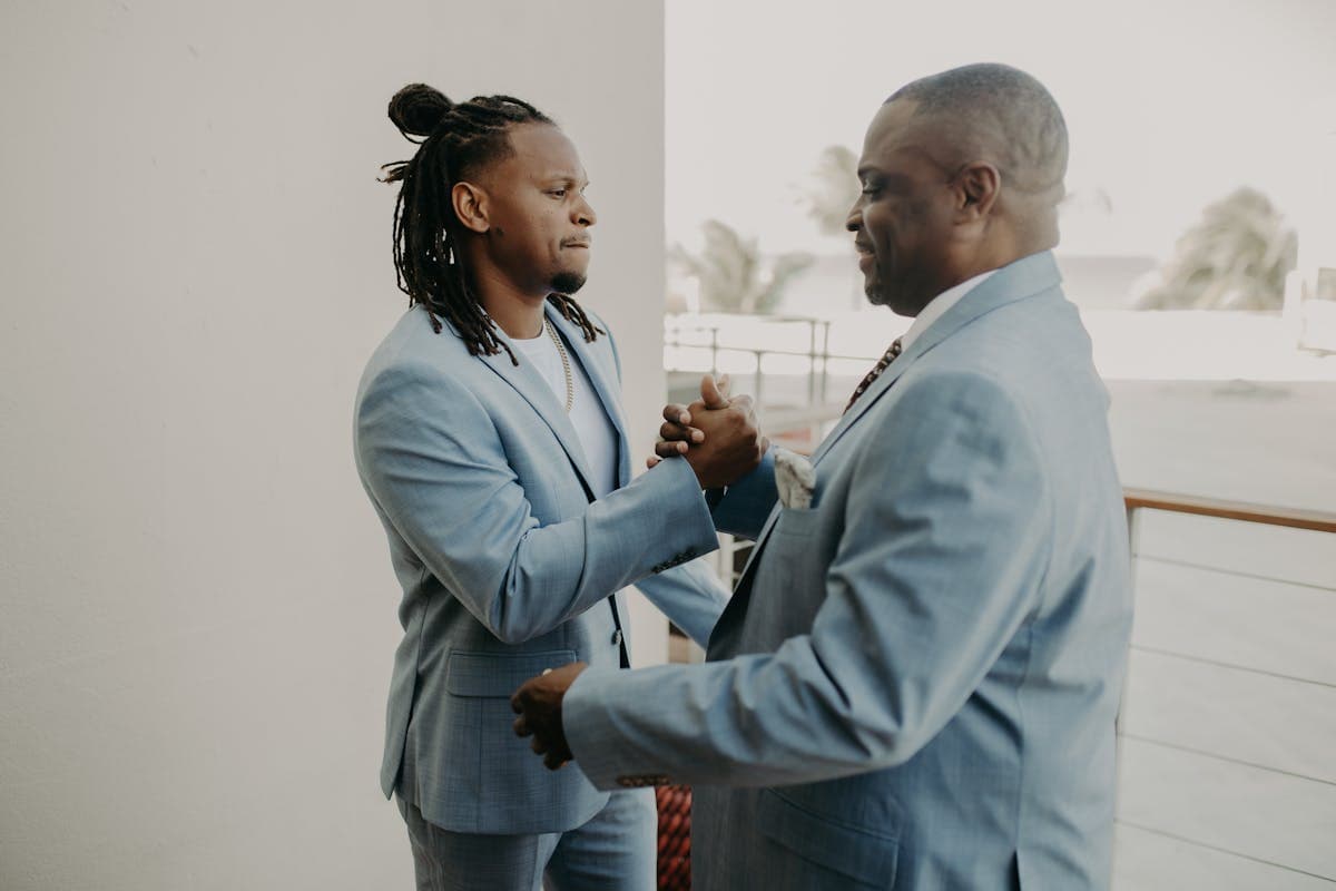 Older father and adult son both in tailored suits standing together at a wedding, dressed in the same family of fabric and accessories