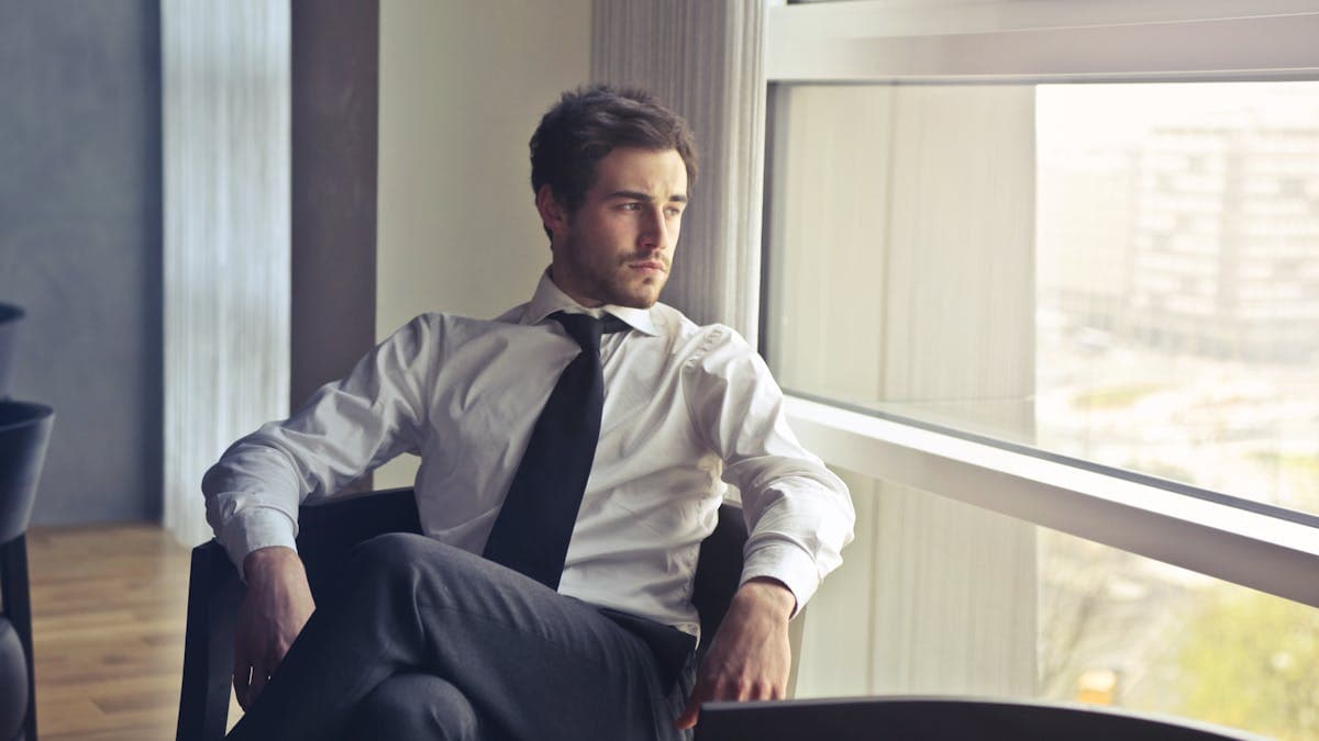 Man in a white dress shirt and tie staring ahead with a distant expression -- the uniform of someone who stopped choosing their clothes a long time ago