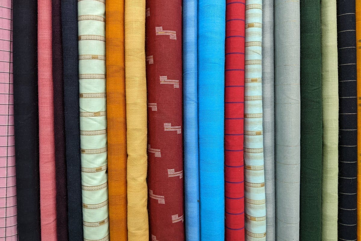 Stacked bolts of wool and blended suiting fabric in a Hoi An tailor's cloth library, sold by named fabric type rather than unverifiable mill claims
