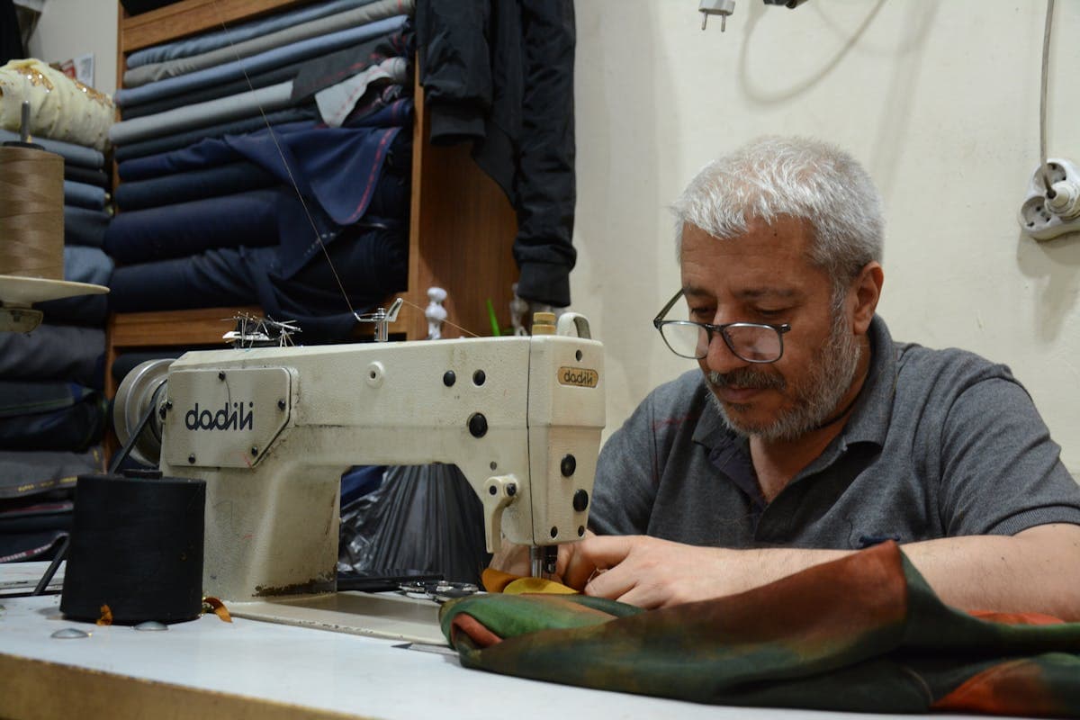 Tailors at sewing machines inside a busy Hoi An workshop, the parallel workforce that lets a single suit be cut, sewn and finished in roughly 24 hours