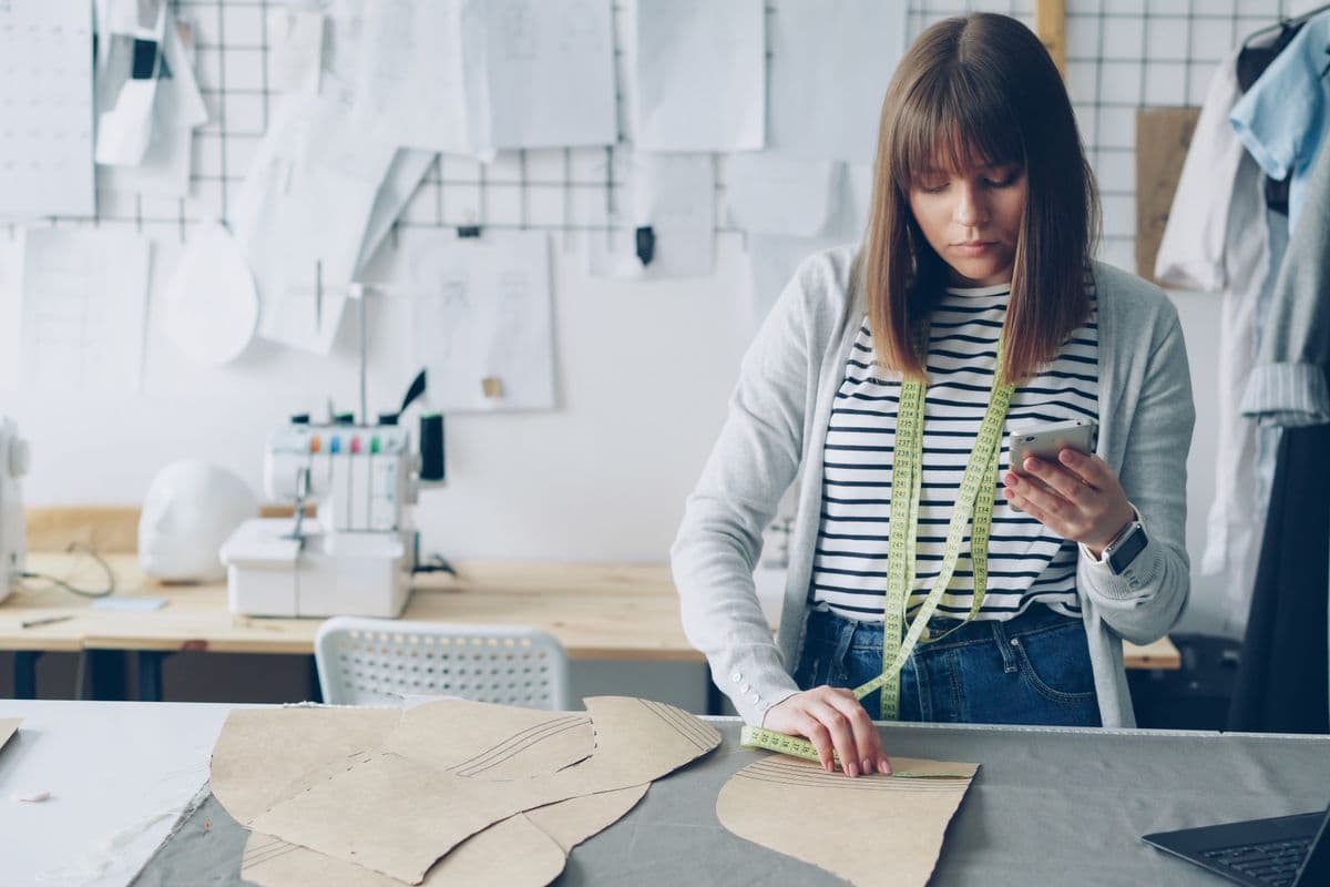 Person using a flexible tape measure at home next to a smartphone, illustrating taking measurements for a remote custom order