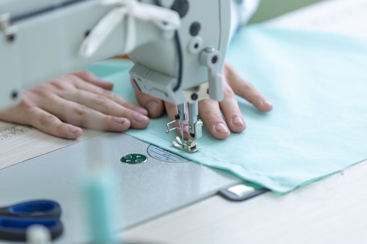 Close-up of a tailor's hands stitching a seam on formal fabric, illustrating the generous seam allowances that let a local tailor adjust the fit