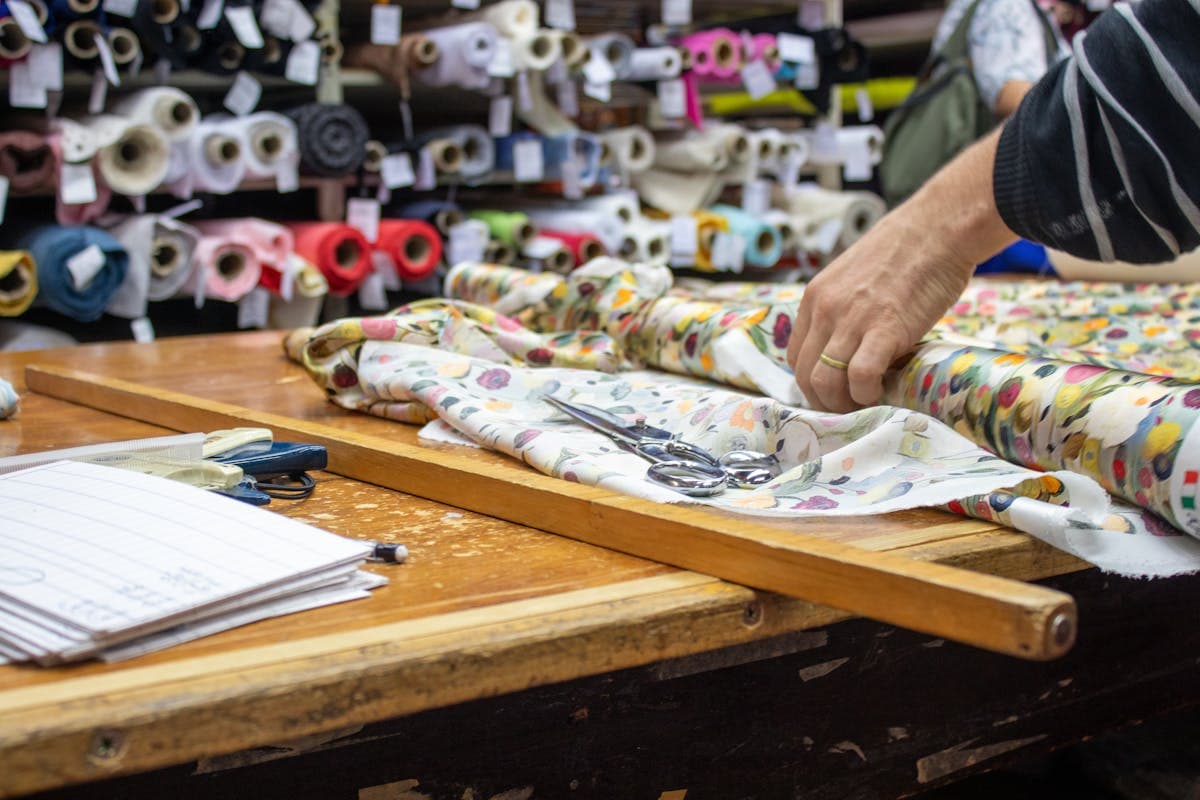 Tailor cutting cloth and working on a half-finished jacket on a workbench in a custom tailoring workshop