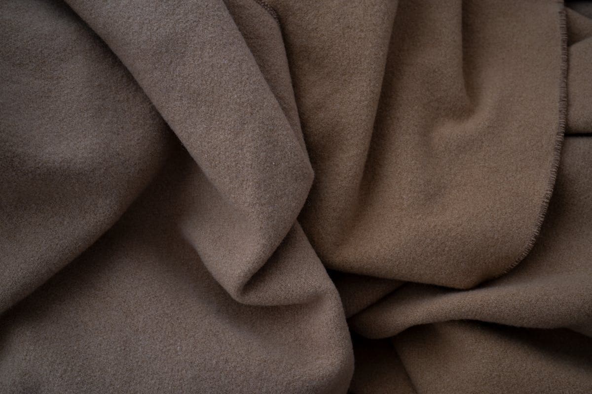 A length of fine worsted wool suiting fabric draping in soft folds, showing the heavier weight and clean drape that white tailoring needs