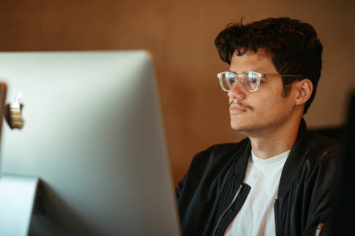 Man hunched over a computer screen at a desk in a shirt, illustrating the forward-lean posture that causes collar gap