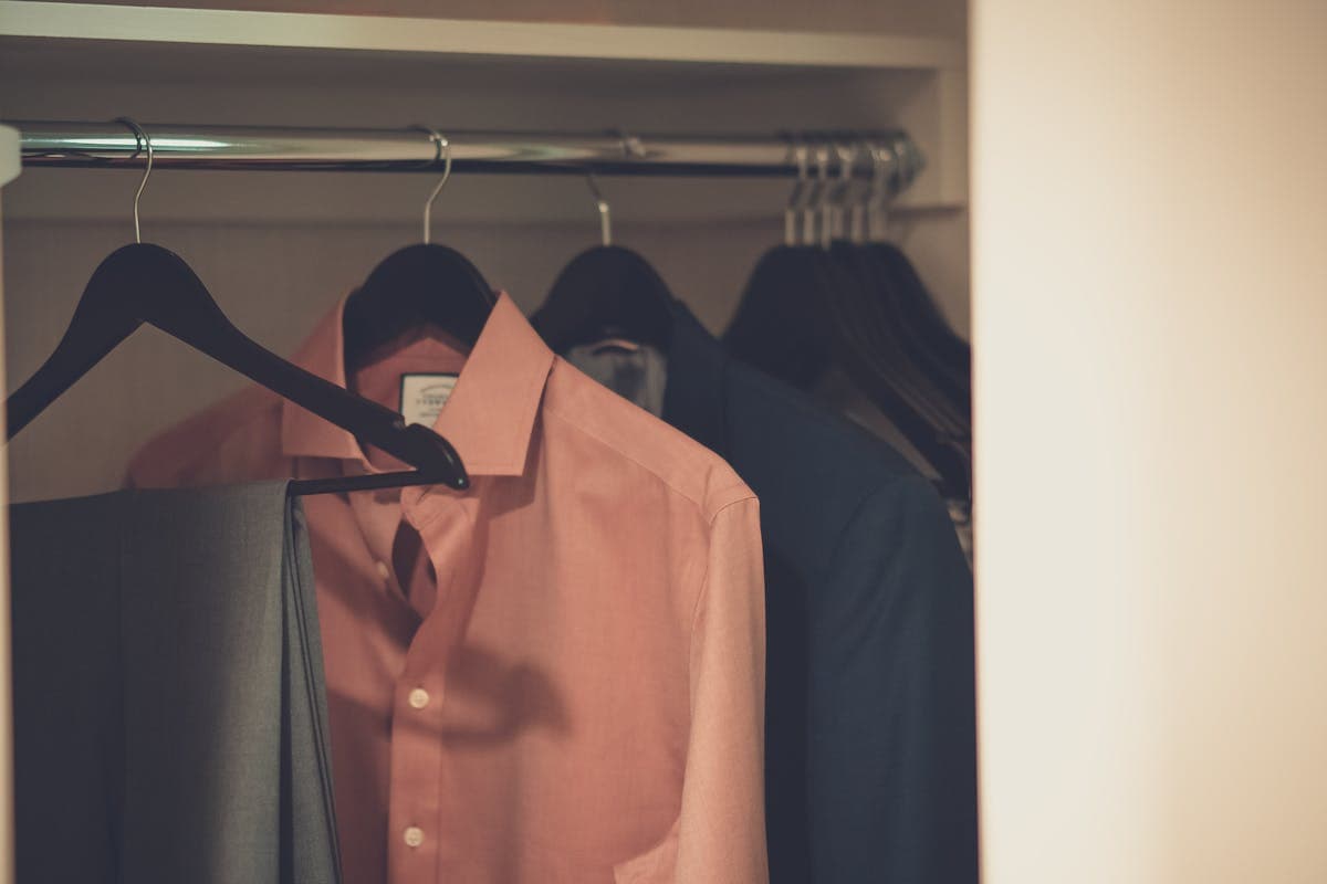 Row of tailored suit jackets of varying lengths hanging on a wooden rack, showing different hem positions
