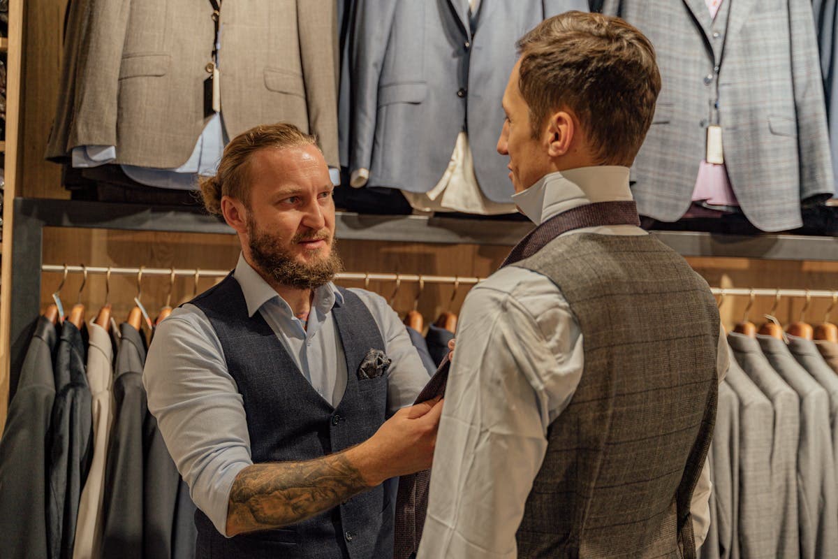 Tailor pinning the sleeve and shoulder of a jacket during a fitting, focus on the upper arm