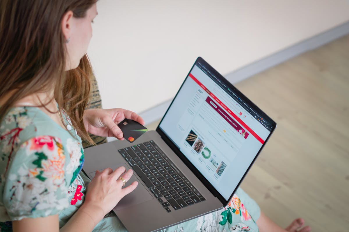 Person browsing an online store on a laptop with a credit card in hand, adding products to a digital cart