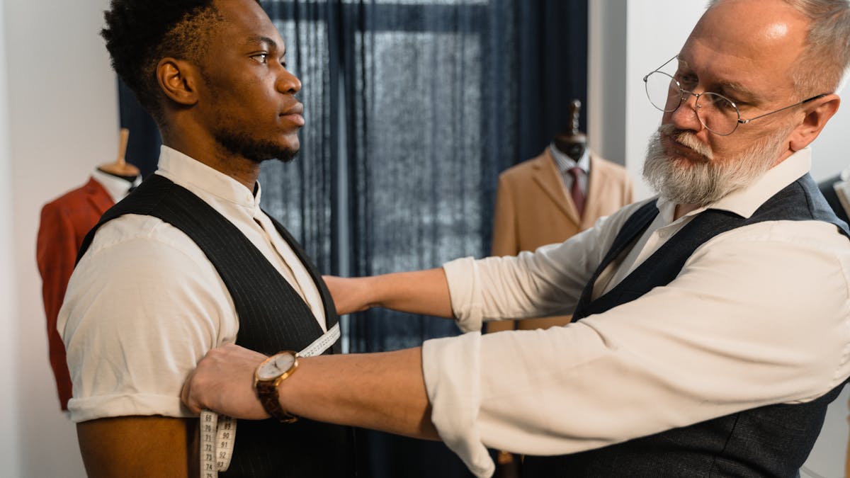 Professional tailor taking precise measurements for a bespoke suit fitting in a tailoring workshop