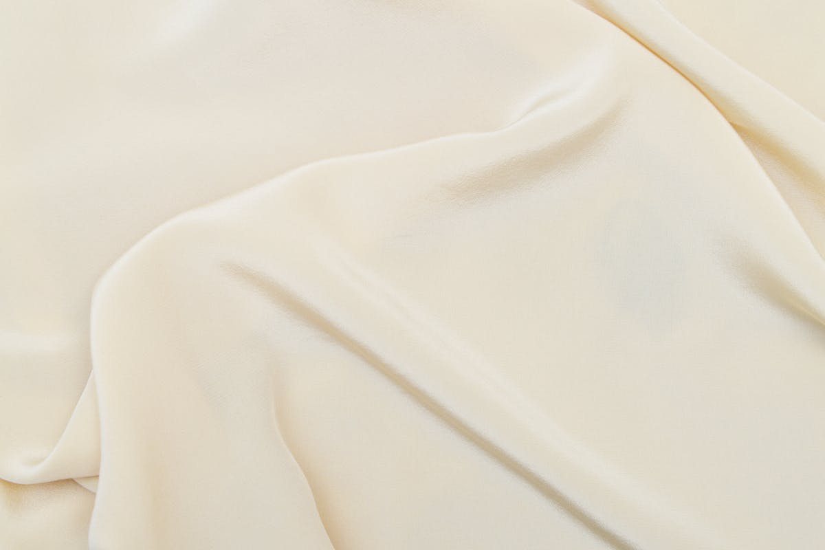 Folds of pearl-white crepe silk and charmeuse fabric showing matte and glossy finishes, the materials used for a custom CBK-style dress