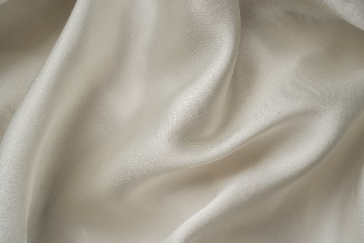 Close-up of smooth mulberry silk fabric draping over skin, showing the soft natural sheen that reduces friction on skin and hair