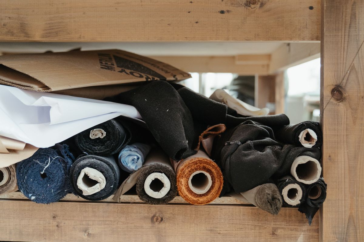 Stacked bolts of fine wool and wool-silk suiting fabric in navy, charcoal and grey on a tailor's shelf