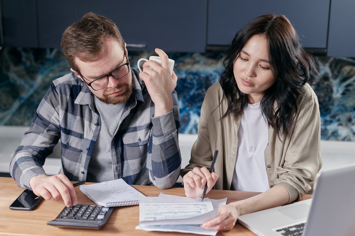 Engaged couple at home reviewing a wedding budget spreadsheet on a laptop with coffee and notebooks