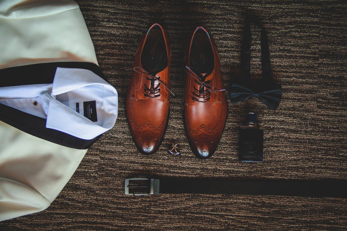 Flat lay of groom accessories: a crisp white shirt, knit silk tie, leather oxford shoes and a folded suit