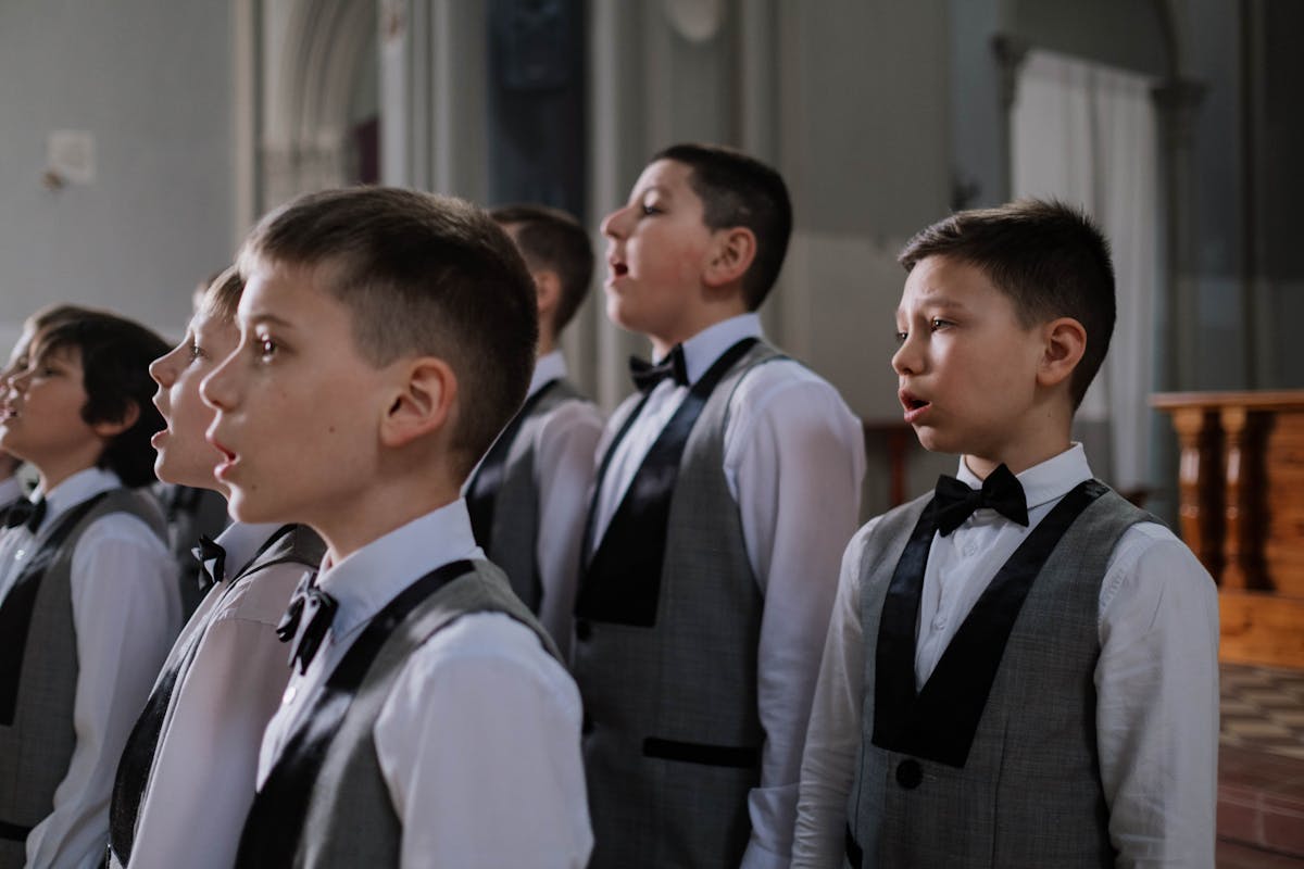 Children walking into a stone church for a First Communion ceremony, boys in dark suits among the group