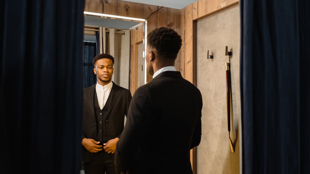 Young man checking his suit fit in a tailor shop mirror, adjusting the jacket shoulder and lapel