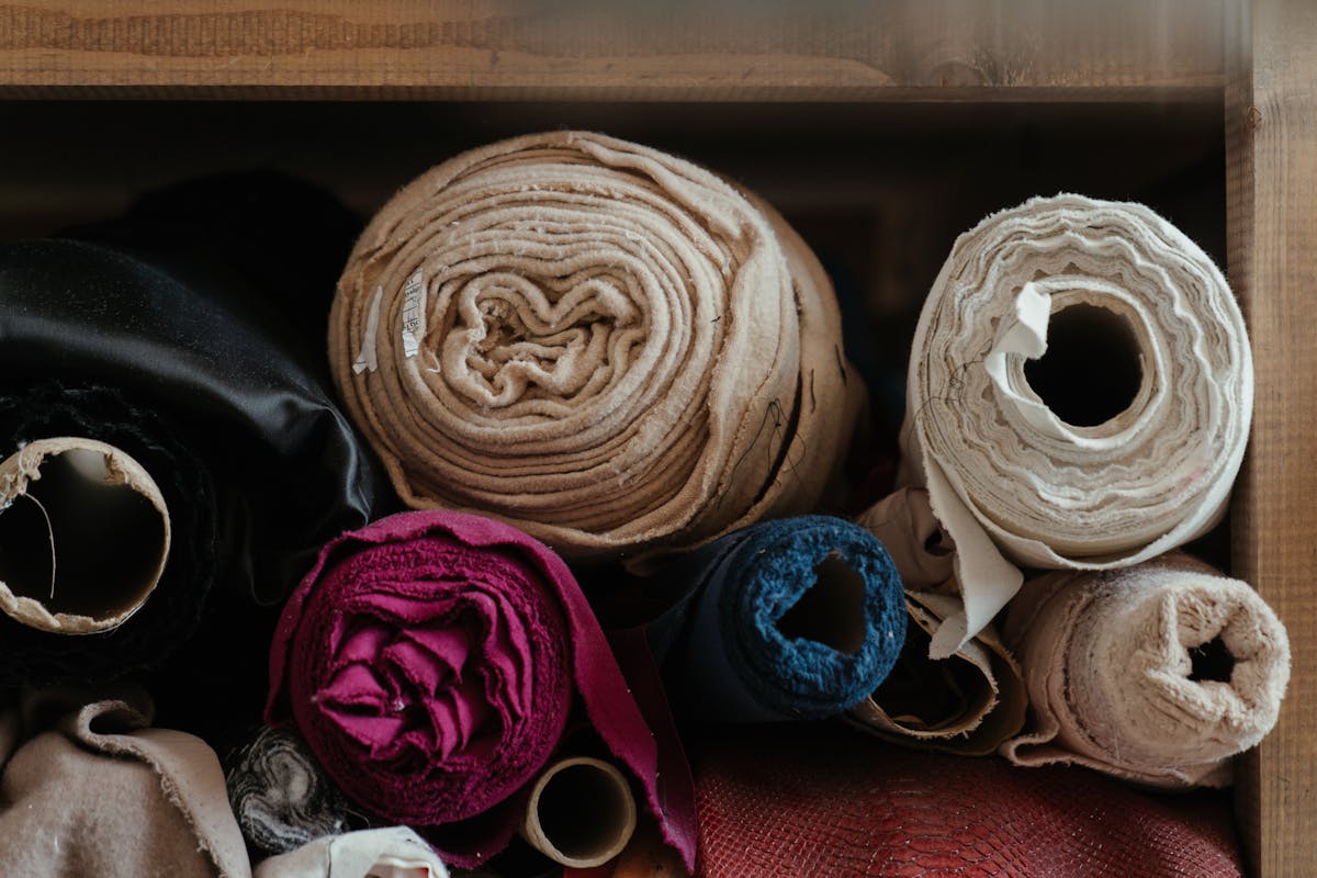 A bolt of charcoal wool suiting cloth rolled on a workshop table under warm light.