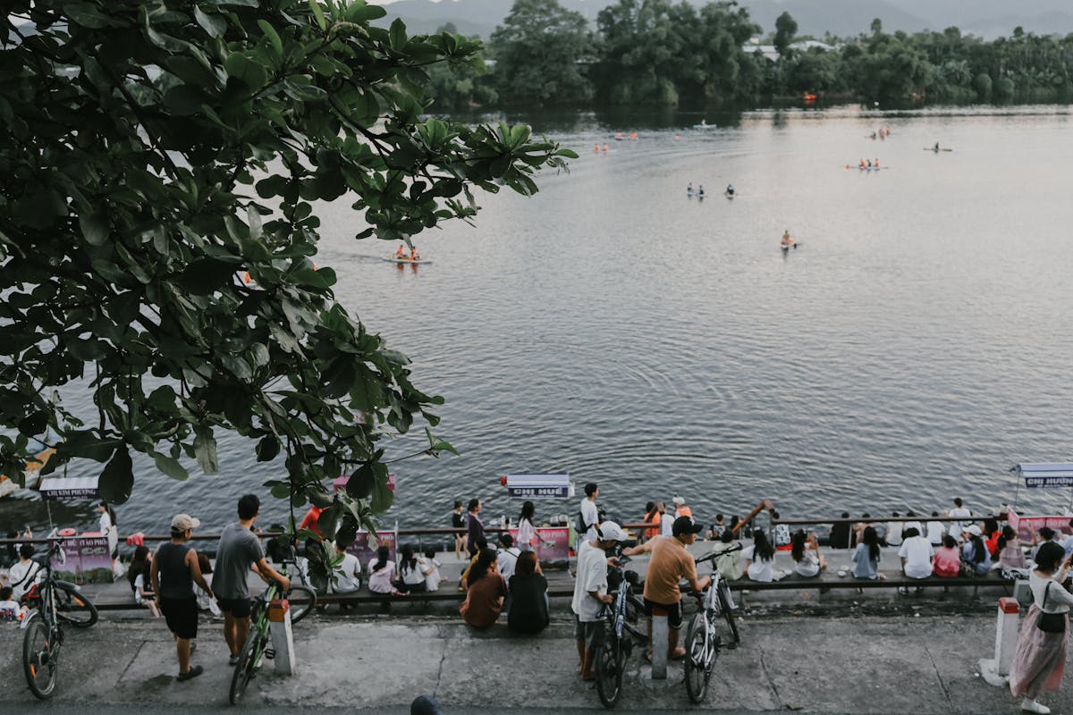Crowd of well-dressed men in blazers and ties watching rowing from a riverside enclosure on a bright summer day