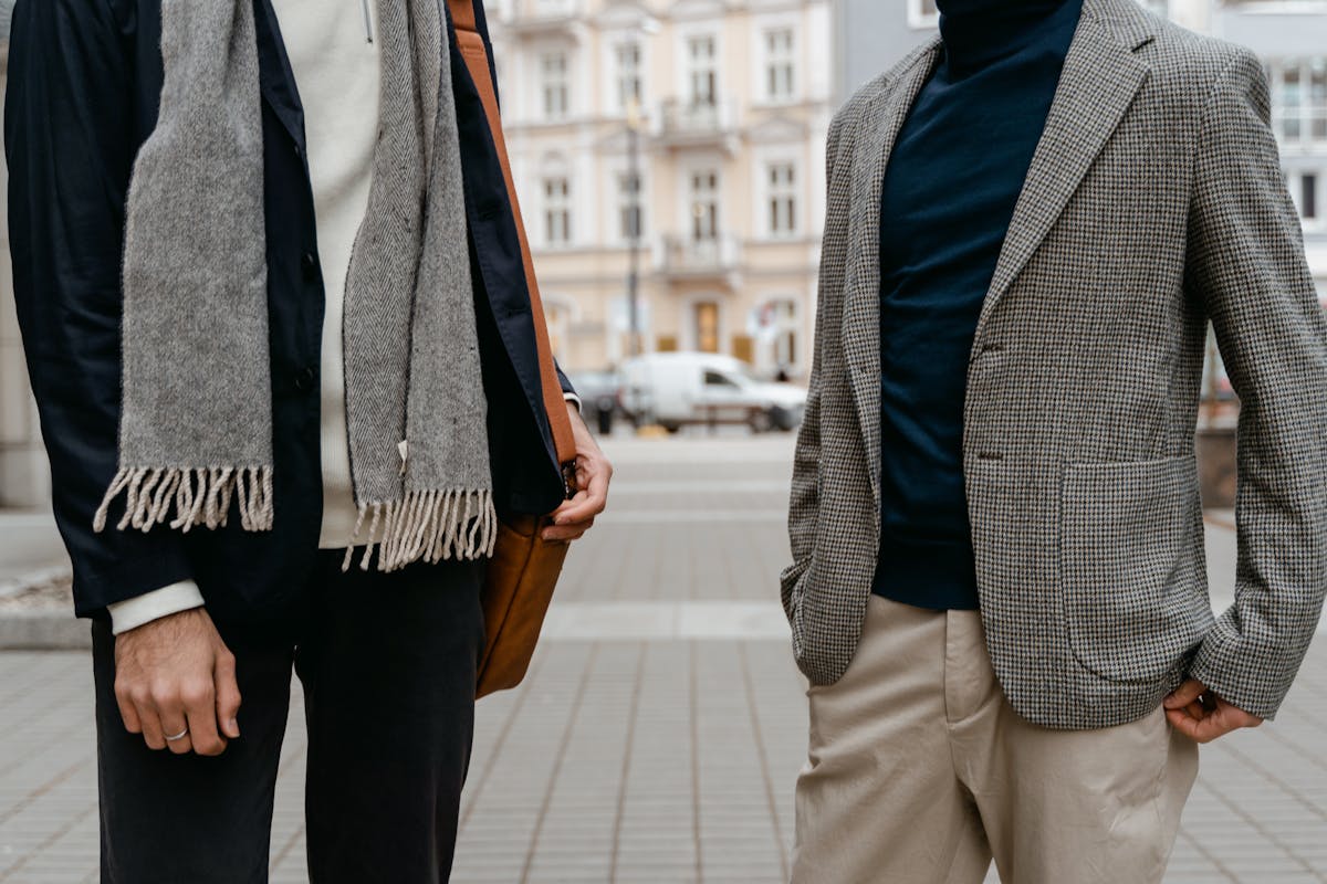 Young man in a navy blazer and chinos with open collar next to a young man in a full matching charcoal suit and tie