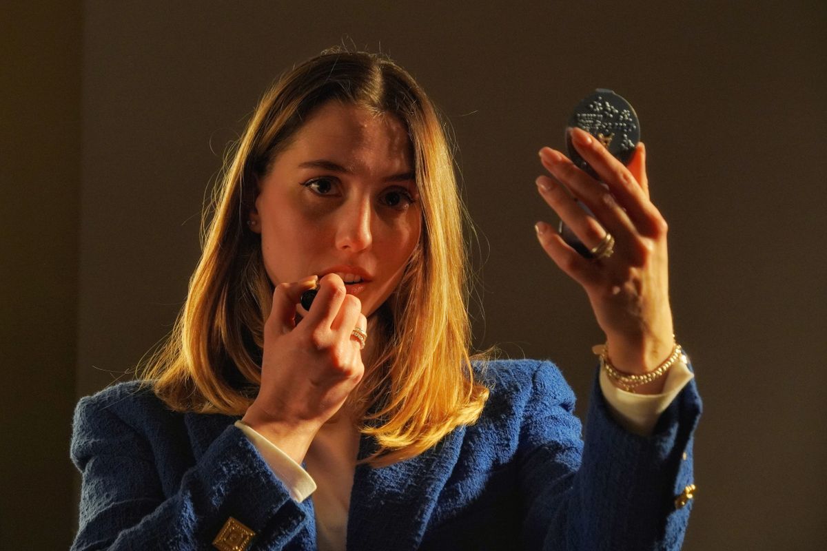 A young woman applying makeup at a mirror while getting ready for an event