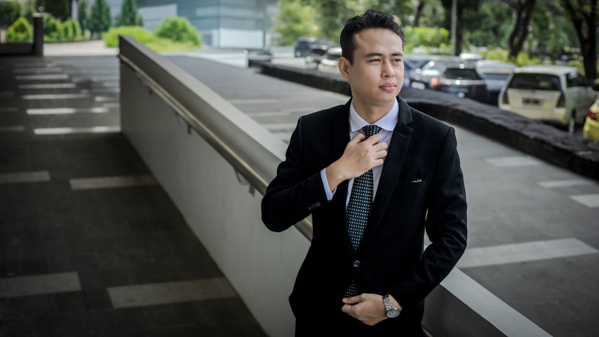 Confident young professional in a well-fitted navy suit adjusting his tie outdoors before a job interview