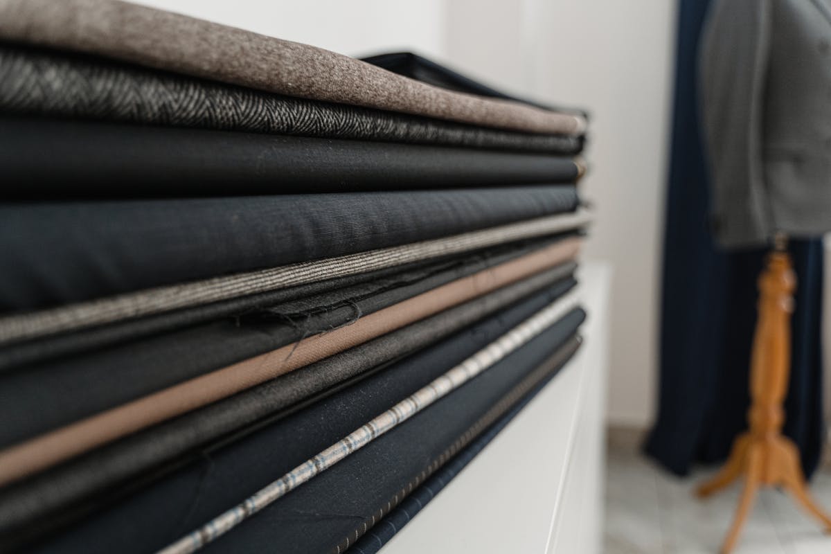 A stack of folded wool suiting fabrics in greys, navy and pinstripe at a tailor shop