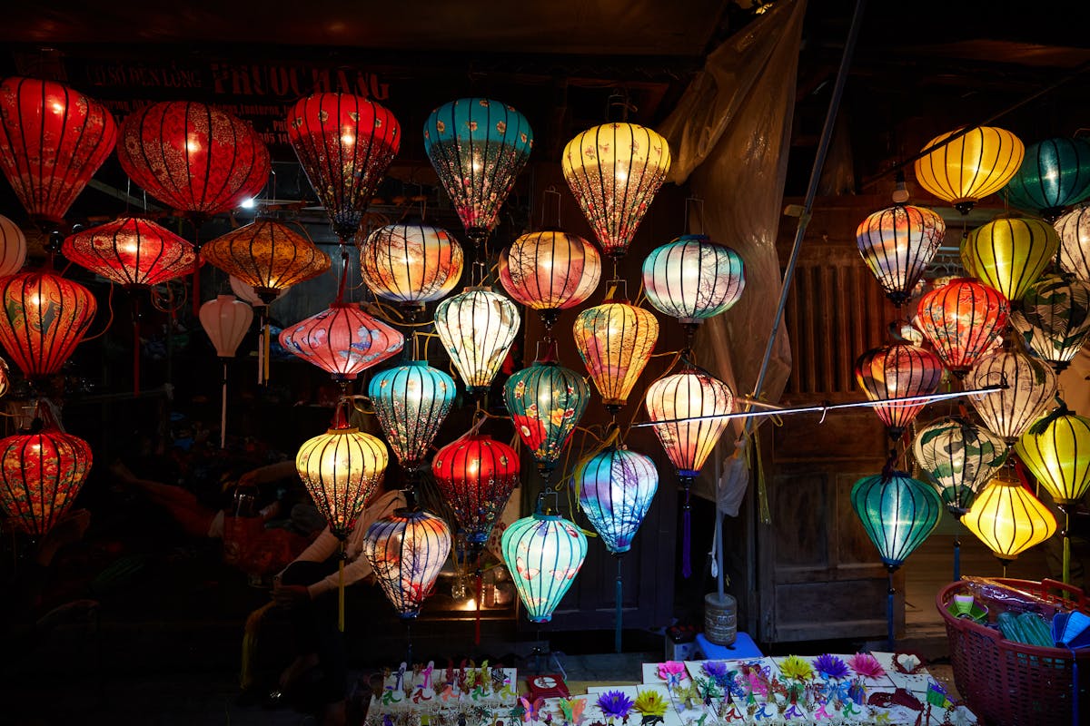 Silk lanterns glowing in every color over a Hoi An street at night, with the river reflecting the lights