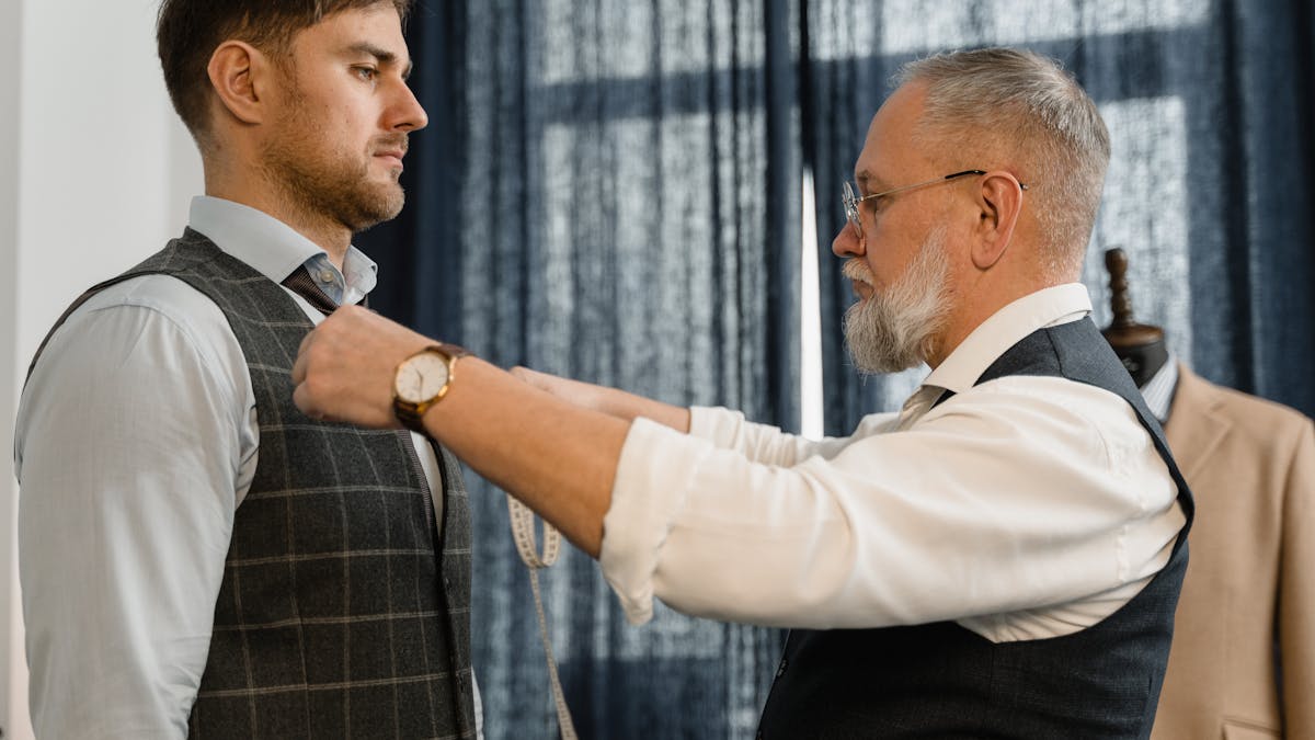 A tailor measuring a client for a custom suit fitting in a workshop -- the same process Australian visitors experience at Nathan Tailors in Hoi An