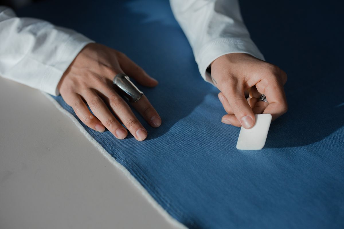 A tailor's worktable scattered with chalk-marked wool, shears, and a half-cut jacket panel inside a traditional workshop