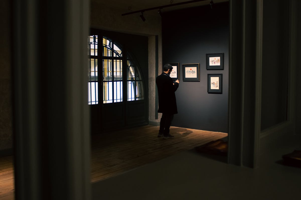 A man in a dramatically lit formal suit standing in a gallery-like space, treating tailoring as art the way the Costume Art theme intends