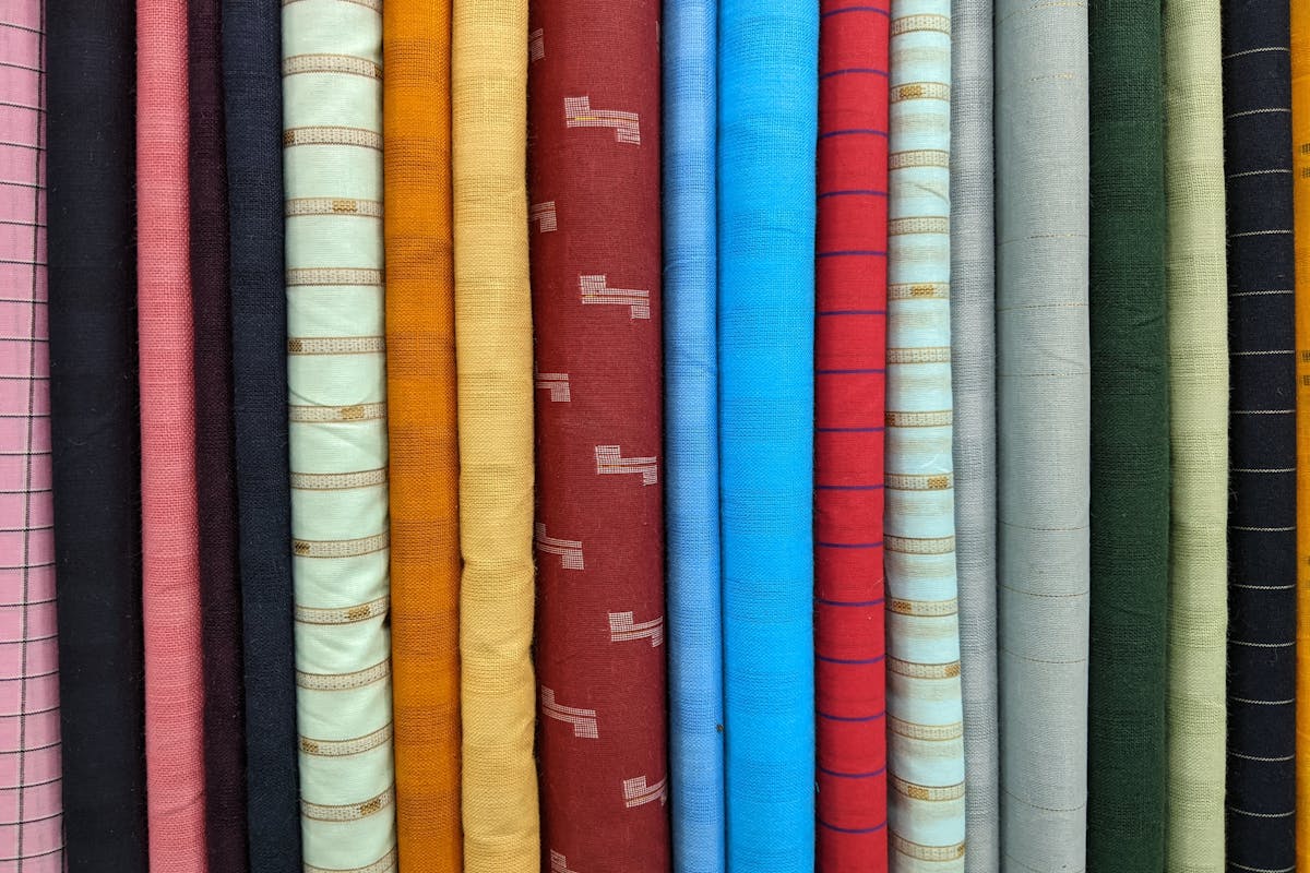 Stacked bolts of wool and blended suiting fabric in a Hoi An tailor's cloth library, sold by named fabric type rather than unverifiable mill claims