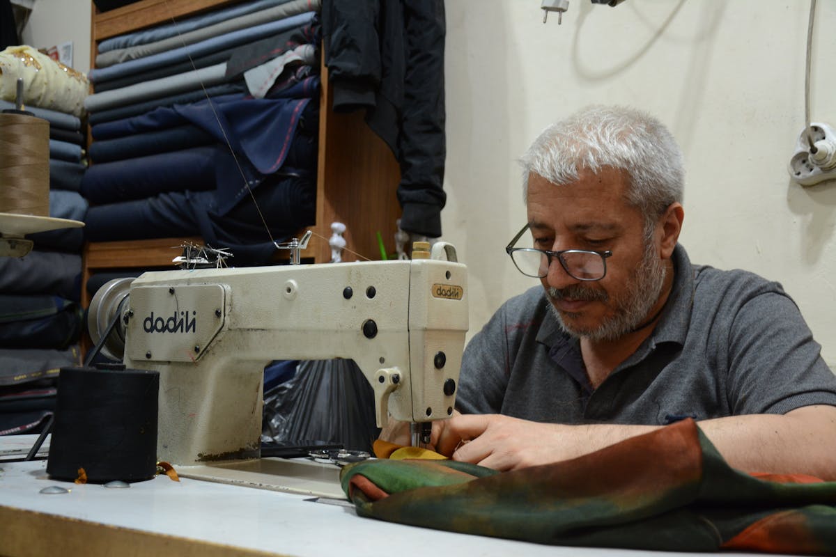 Tailors at sewing machines inside a busy Hoi An workshop, the parallel workforce that lets a single suit be cut, sewn and finished in roughly 24 hours