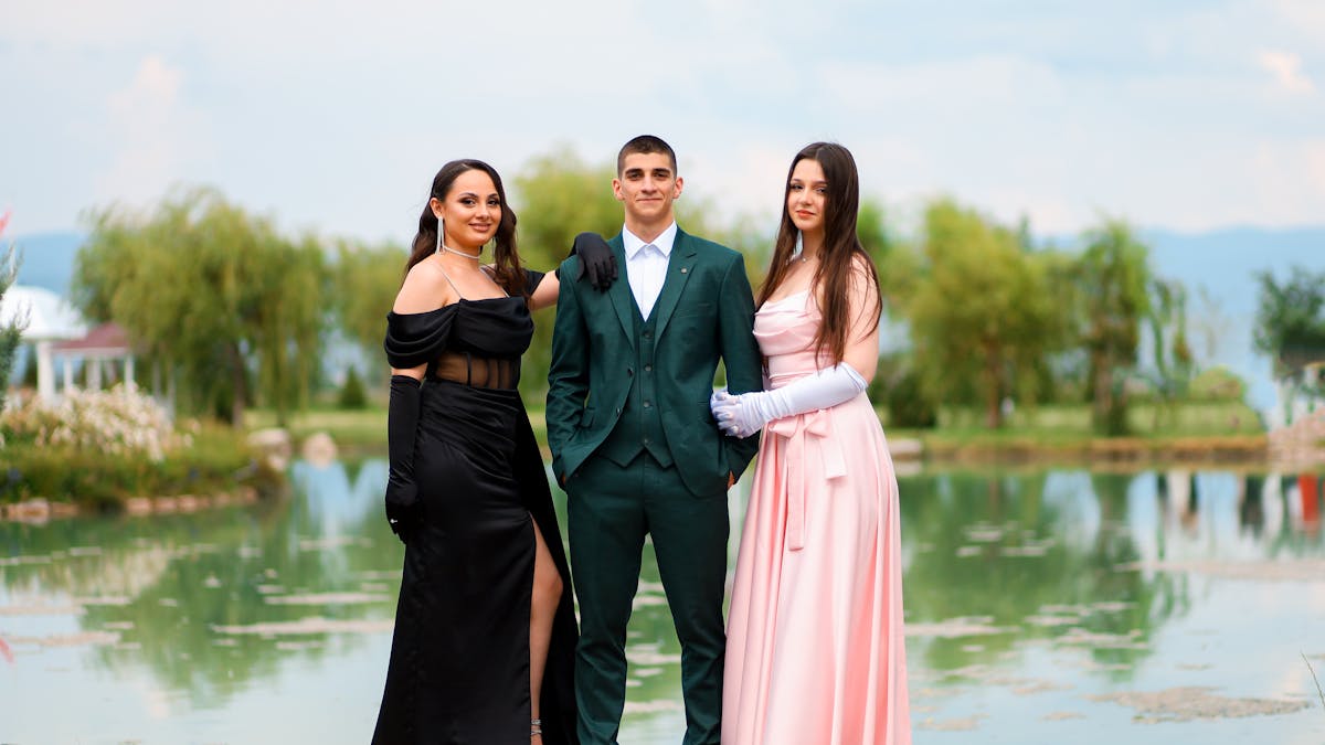 Elegantly dressed young adults in formal suits posing by a scenic lakeside