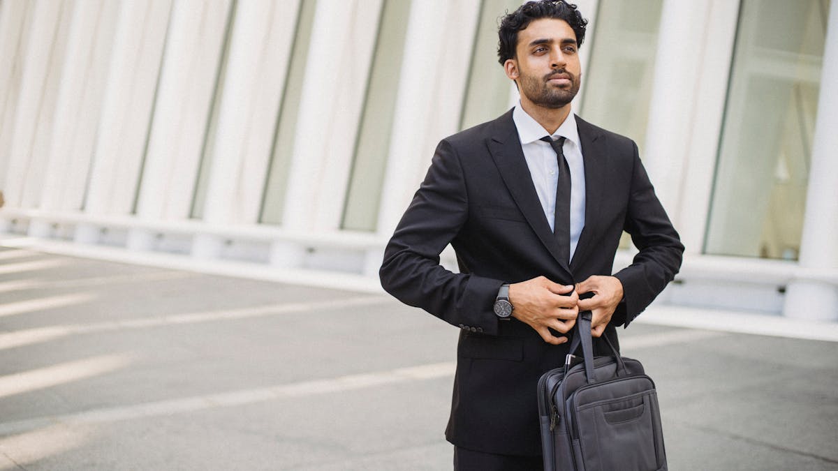 Professional man in a suit buttoning his jacket outside a modern office building -- the return-to-office reality that millions of NYC workers are facing in 2026
