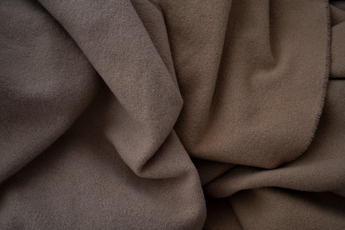 A length of fine pure wool suiting fabric draping in soft folds, showing the heavier weight and clean drape that white tailoring needs