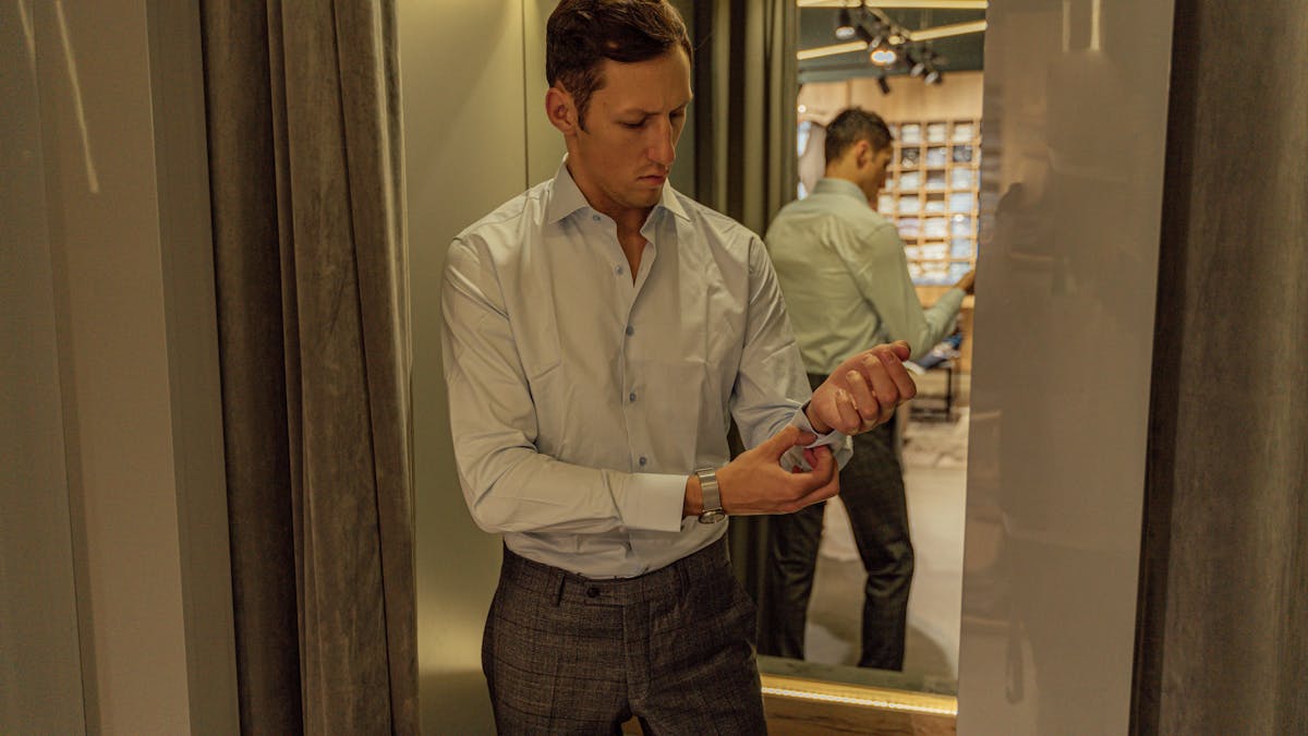 Man checking suit fit in a full-length mirror -- the jacket shoulders align perfectly and the trouser break is clean