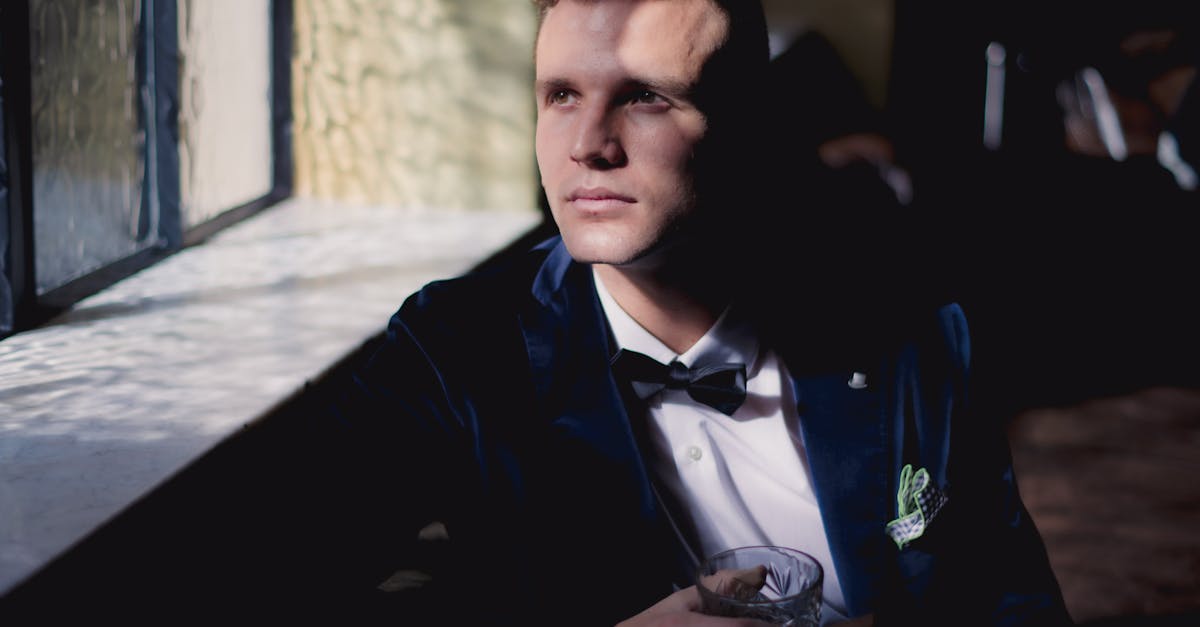 Groom in a deep green velvet dinner jacket and black tuxedo trousers standing beside a stone fireplace, photographed in low warm light