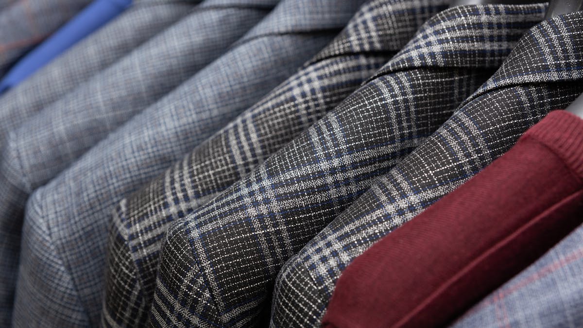 Classic men's suits in different colors and patterns hanging on a wardrobe rack, showcasing the range of suit color options from navy to charcoal to earth tones