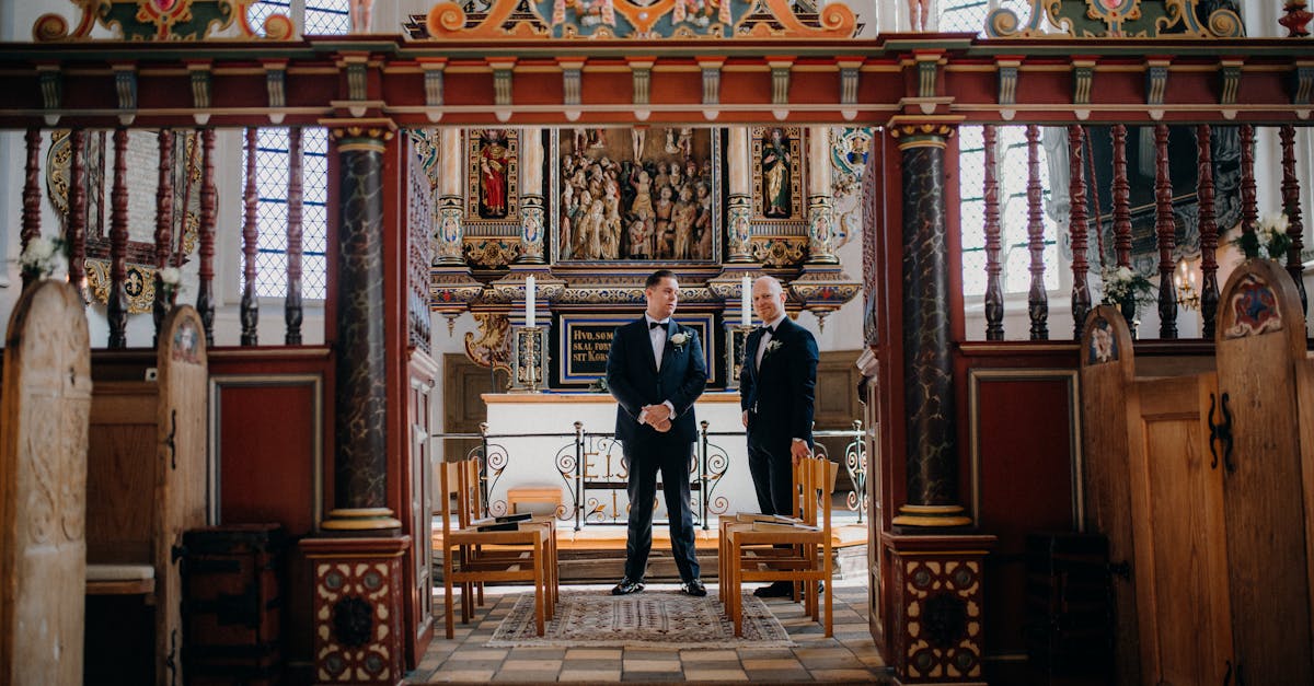 A groom and best man at a softly lit altar, in tailored formalwear with subtle differentiation between the two looks.