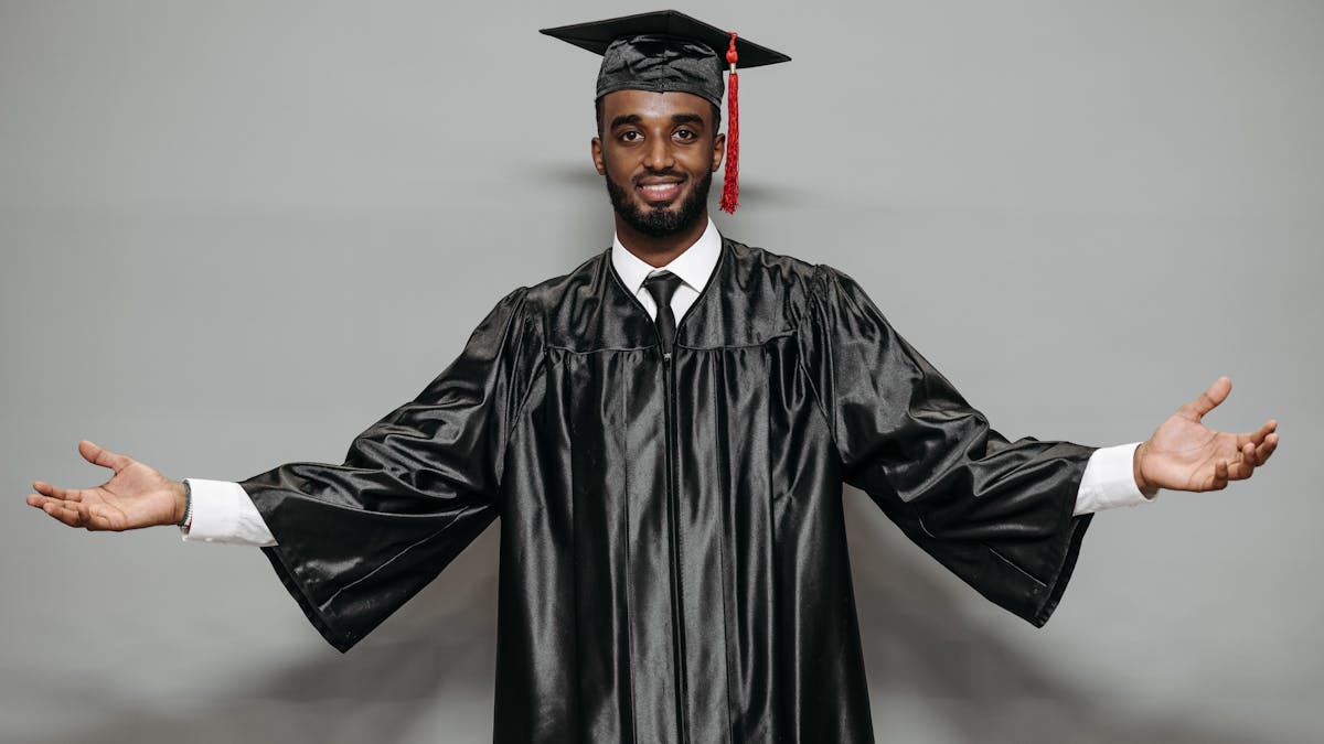 Young man in graduation cap and gown celebrating his achievement with a confident smile -- the right outfit underneath makes all the difference