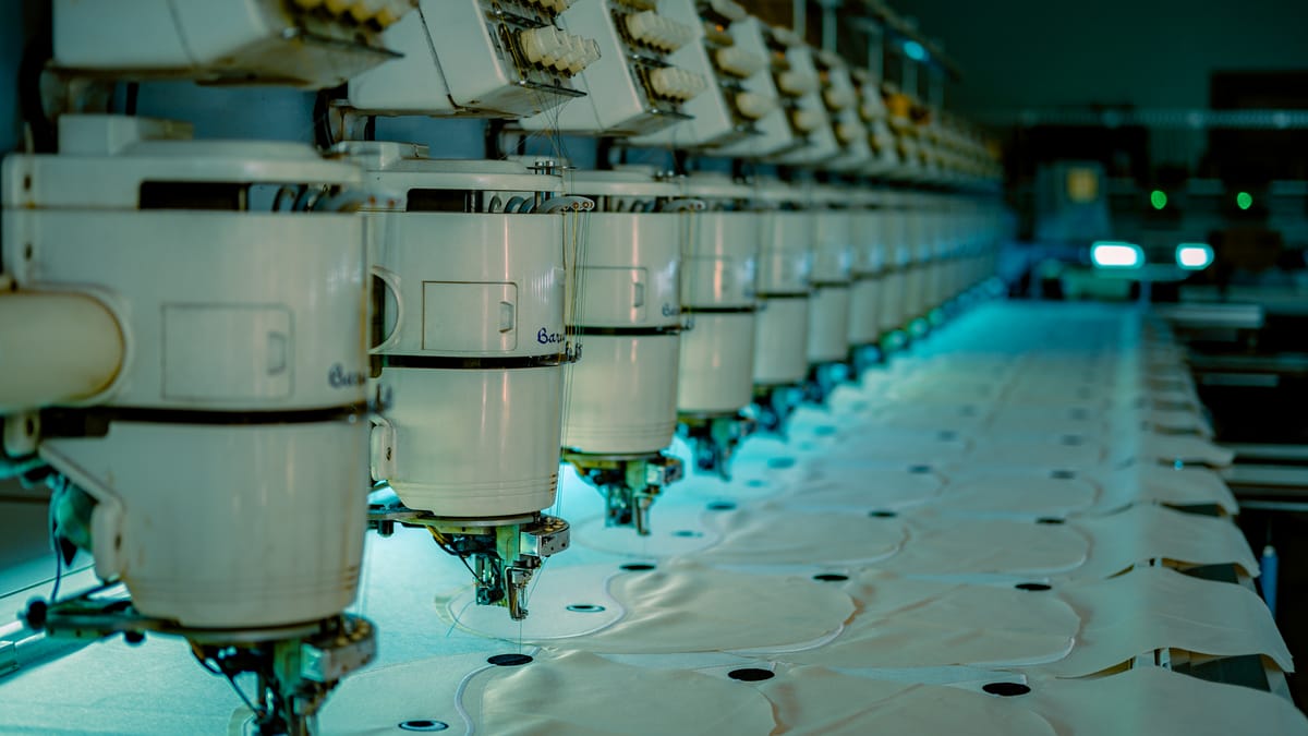 A long row of industrial sewing machines on a garment factory floor — where most off-the-rack suits sold in the US are produced