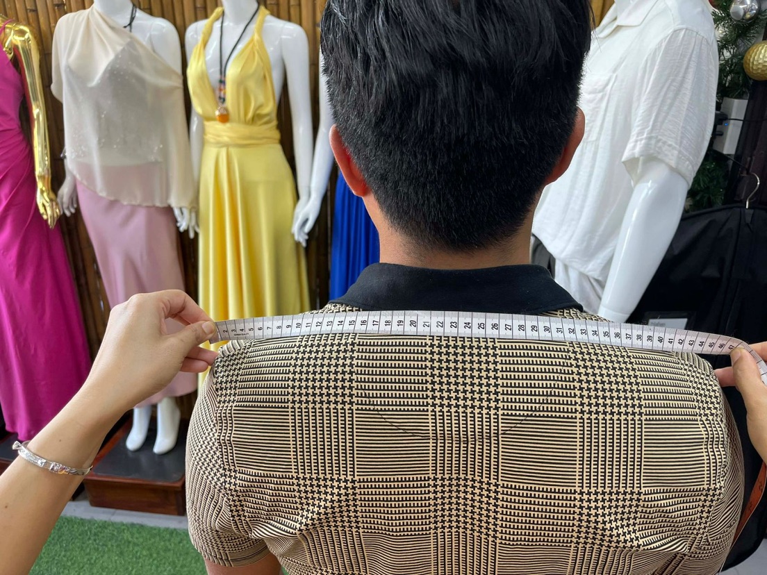 A Nathan Tailors master tailor measuring shoulder width by hand across a customer's back in the Hoi An shop